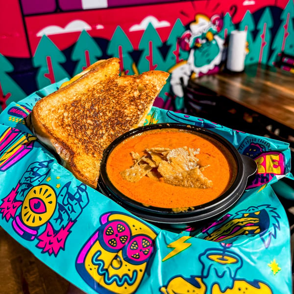 Grilled cheese and tomato soup with tortilla strips in a colorful basket against a vibrant mural.