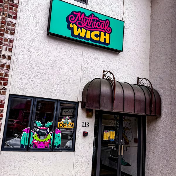 Exterior of Mythical 'Wich restaurant with a vibrant sign, window decals, and an awning.