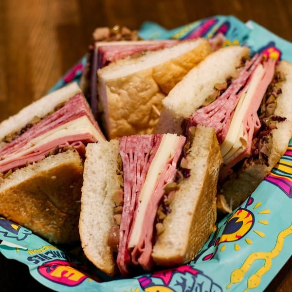 Several deli sandwiches with meat, cheese, and olive salad, served in a colorful paper liner.