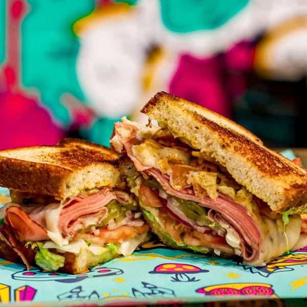 A large, toasted sandwich filled with deli meat, cheese, lettuce, tomatoes, and pickles.