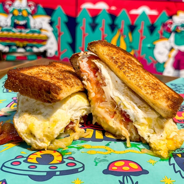 A grilled cheese sandwich with egg and bacon, cut in half, on a colorful placemat.